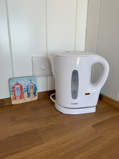 An electric kettle plugged in on the worktop beside a beach hut coaster.